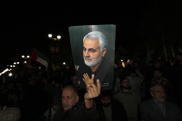 A demonstrator holds up a poster of the late Iranian Revolutionary Guard Gen. Qassem Soleimani, who was killed in a U.S. drone attack in 2020 in Iraq, during an anti-Israeli gathering in front of the British Embassy in Tehran, Iran, early Sunday, April 14, 2024. Iran launched its first direct military attack against Israel on Saturday. (AP Photo/Vahid Salemi)
