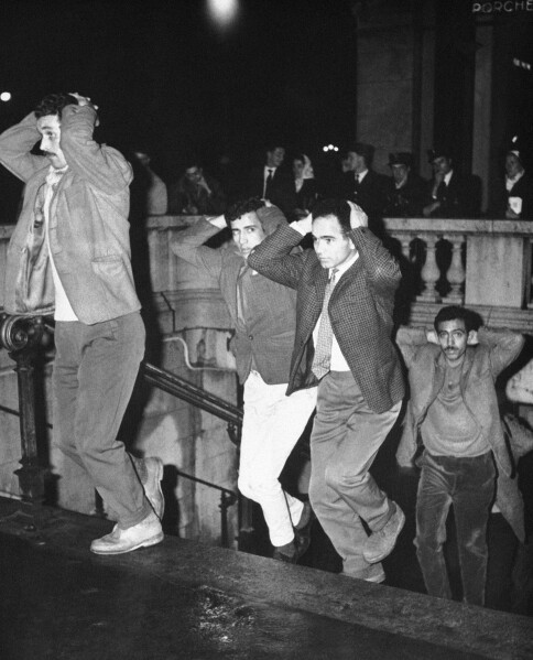 FILE - Men come out of Paris subway station with their hands on their heads after being arrested in Paris, Oct. 17, 1961, for failure to obey curfew imposed on Algerians. Algerians and wounding at least four. French lawmakers on Thursday March 28, 2024 condemned an infamous 1961 police crackdown on Algerian protesters in Paris as a "bloody and murderous repression," marking another step in the country's recognition of the massacre that authorities sought to cover up for decades. (AP Photo, File)