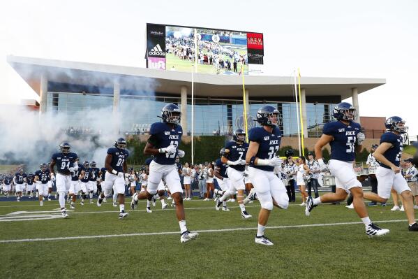 FILE - In this Sept. 6, 2019, file photo, Rice University football players run onto the field for an NCAA football game in Houston.  The Wild West nature of the upcoming college football season can be illustrated in part by 160 miles of Texas highway that connects the trendy college city of Austin with the bustling metropolis of Houston. (AP Photo/Matt Patterson, File)