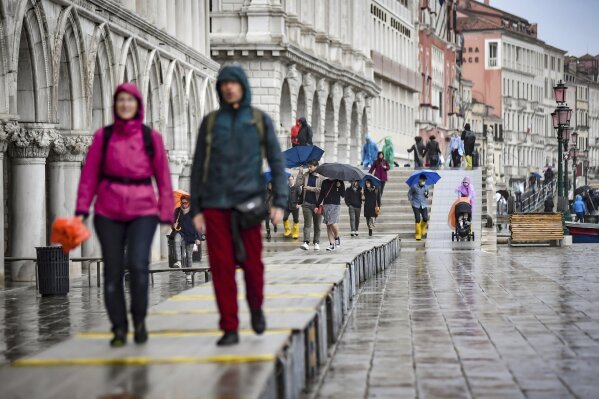 Visitors walk on on a trestle bridges during an expected high water, in Venice, northern Italy, Saturday, Oct. 3, 2020. Controversial and long-delayed underwater barriers passed their first emergency with flying colors on Saturday, protecting the Italian lagoon city of Venice from a tide that peaked at 130 centimeters (51-inches), a level that would normally inundate about half of the city.  (Claudio Furlan/LaPresse via AP)