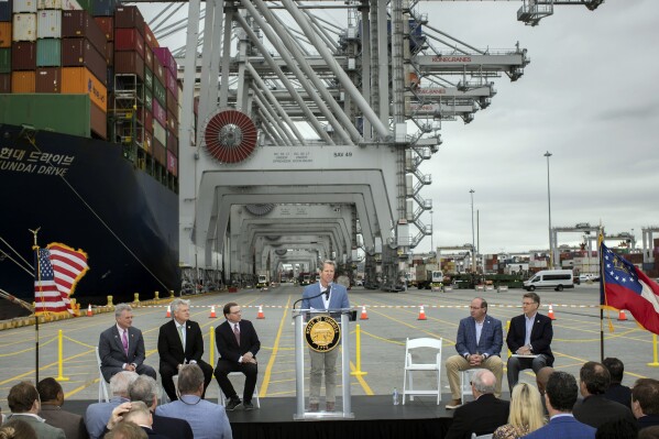 In this photo provided by the Georgia Port Authority, Georgia Gov. Brian Kemp, center, speaks during a visit to the Port of Savannah with U.S. Reps. Sam Graves, R-Ga., center left, Buddy Carter, R-Ga., left, and Mike Collins, R-Ga., center left, at the Georgia Ports Authority's Garden City Terminal, Monday, March, 25, 2024, in Savannah, Ga. The Georgia Ports Authority has been pushing for Congress to consider another round of deepening Savannah’s shipping channel. The agency’s leaders say ever-growing classes of enormous cargo ships need even deeper water to be able to reach the port with full loads during lower tides. (Stephen B. Morton/Georgia Port Authority via AP)