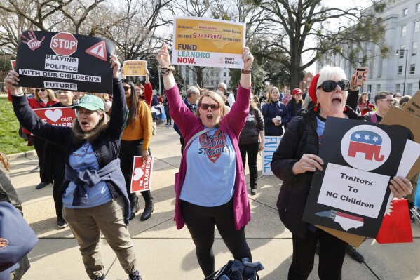 Sara Juhl from Weddington, from left, Jen Sanders from Waxhaw and Meg Bell from Monroe cheer on speakers during a rally for education funding on the grounds of the North Carolina State Capitol in Raleigh, N.C., Thursday, Feb. 22, 2024. The rally happened as the state Supreme Court heard oral arguments in the long-running Leandro school funding case. (Ethan Hyman/The News & Observer via AP)