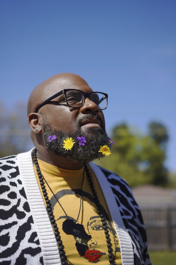 Lama Rod Owens poses for a portrait with his beard covered in flowers in the yard of his childhood home in Rome, Georgia on Saturday, March 30, 2024. Owens is an influential voice in a new generation of Buddhist teachers, respected for his work focused on social change, identity and spiritual wellness. His latest book is entitled "The New Saints," which highlights Christian saints and spiritual warriors, Buddhist bodhisattvas and Jewish tzaddikim among those who have sought to free people from suffering. (AP Photo/Jessie Wardarski)