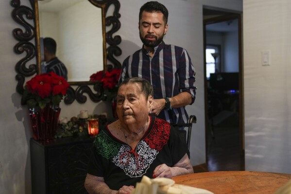 Joaquin Sanchez plays with the hair of his grandmother Aurora Sandoval as they wait for the next step in tamale-making with family members at the family home Tuesday, Dec. 26, 2023, in Chicago. When she was 1, Noelia Sanchez and her mother Aurora, who had no work documents, were rounded up with dozens of other immigrants in a Texas town near the border. The U.S.-born child and her mother were forced to go to Mexico along with hundreds of thousands of other people. (AP Photo/Erin Hooley)