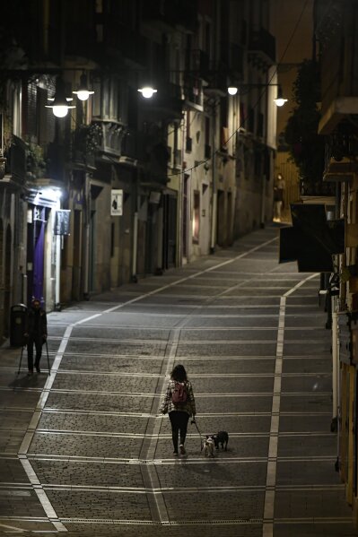 A resident walks with a dog along an empty Curia street, in Pamplona, northern Spain, Saturday, Oct. 24, 2020, as new measures against the coronavirus began in the Navarra province where all bar and restaurants are closed for 15 days from midnight Wednesday.  (AP Photo/Alvaro Barrientos)