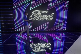 FILE - A worker walks past neon signs for Ford at the Auto Shanghai 2023 show in Shanghai, Tuesday, April 18, 2023. Ford reports their earnings on Wednesday, April 24, 2024. (AP Photo/Ng Han Guan, File)