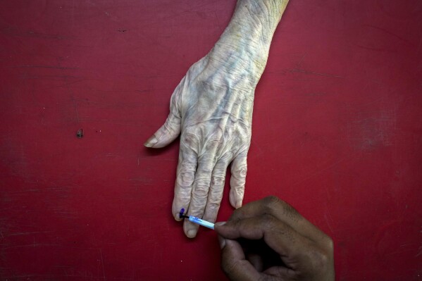 文件——2024年4月28日，星期日，印度古瓦哈蒂，一名民意调查官员在89岁的鲁比·保罗的住所用邮政选票投票后，将不可磨灭的墨水印在她的食指上。（美联社照片/Anupam Nath）