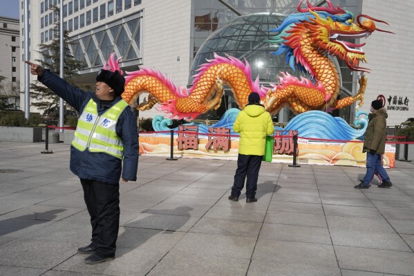 A municipal worker gives direction near a sculpture of a dragon in Beijing, Saturday, March 2, 2024. One burning issue dominates as the 2024 session of China's legislature gets underway this week: the economy. The National People's Congress annual meeting, which opens Tuesday, is being closely watched for any signals on what the ruling Communist Party might do to re-energize an economy that is sagging under the weight of expanded government controls and the bursting of a real-estate bubble. (AP Photo/Ng Han Guan)