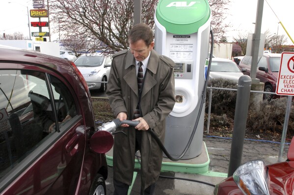 FILE - Thomas Miller, Western EV fleet sales manager for Mitsubishi Motors North America, demonstrates a fast-charger connection on a Mitsubichi i car Friday, March 16, 2012 in Central Point, Ore. The second-largest electric vehicle fast-charging network, Electrify America, with 800 direct-current fast-charging stations and more than 3,600 plugs nationwide, said Wednesday, July 26, 2023, it will work to add Tesla's connector to existing and future chargers by 2025. (AP Photo/Jeff Barnard, File)