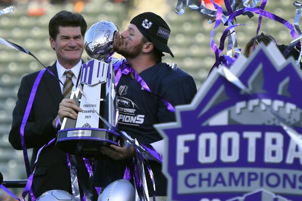Craig Thompson, Mountain West Conference commissioner, stands next to Utah State quarterback Logan Bonner (1) who kisses the trophy after defeating San Diego State during an NCAA college football game for the Mountain West Conference Championship, Saturday, Dec. 4, 2021, in Carson, Calif. (AP Photo/John McCoy)