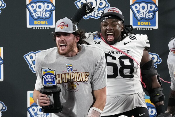 MVP Iowa State quarterback Rocco Becht, left, celebrates with his trophy as teammate defensive lineman J.R. Singleton (58) cheers after Iowa State defeated Miami in the Pop Tarts Bowl NCAA college football game, Saturday, Dec. 28, 2024, in Orlando, Fla. (AP Photo/John Raoux)