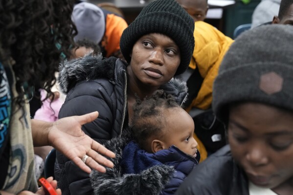 FILE - Haitian immigrant Rose Juliane, center, holds her daughter Rosie Sarah, as she speaks with Immigrant Family Services Institute Executive Director Geralde Gabeau, left, while waiting at the agency in the Mattapan neighborhood of Boston for transportation to a shelter, Thursday, Nov. 16, 2023. Massachusetts has begun awarding grants to local agencies to set up temporary housing sites for homeless families as officials grapple with finding newly arriving migrants places to stay after hitting a state-imposed limit of 7,500 families in the state’s emergency homeless shelter system. (AP Photo/Steven Senne, File)