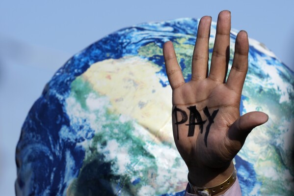 file - one hand reads "Salary" Calling for compensation for losses and damages at the COP27 UN climate summit in Sharm el-Sheikh, Egypt on Friday, November 18, 2022.  (AP Photo/Peter DeJong, File)
