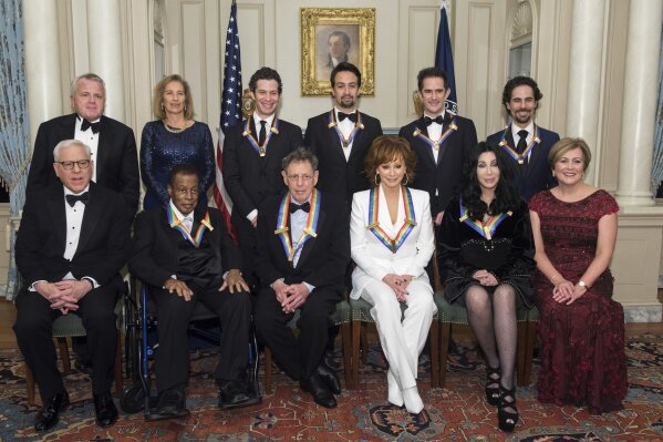 
              Front row from left, David Rubenstein, 2018 Kennedy Center Honorees Wayne Shorter, Philip Glass, Reba McEntire, Cher, Kennedy Center President Deborah Rutter; back row from left, Deputy Secretary of State John Sullivan, Grace Rodriguez, and the 2018 Kennedy Center Honorees, the co-creators of "Hamilton," Thomas Kail, Lin-Manuel Miranda, Andy Blankenbuehler, and Alex Lacamoire pose for the group photo at the State Department following the Kennedy Center Honors State Department Dinner on Saturday, Dec. 1, 2018, in Washington. (AP Photo/Kevin Wolf)
            