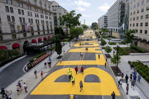 The Washington Monument and the White House are visible behind the words Black Lives Matter sign that has been painted in bright yellow letters on the 16th Street by city workers and activists, Friday, June 5, 2020, in Washington. (Khalid Naji-Allah/Executive Office of the Mayor via AP)