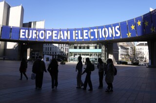 FILE - A group stands under an election banner outside the European Parliament in Brussels on April 29, 2024. In an increasingly vitriolic political climate, the last thing needed in the runup to the June European Union elections was an assassination attempt on one of the bloc’s most controversial figures. (AP Photo/Virginia Mayo, File)
