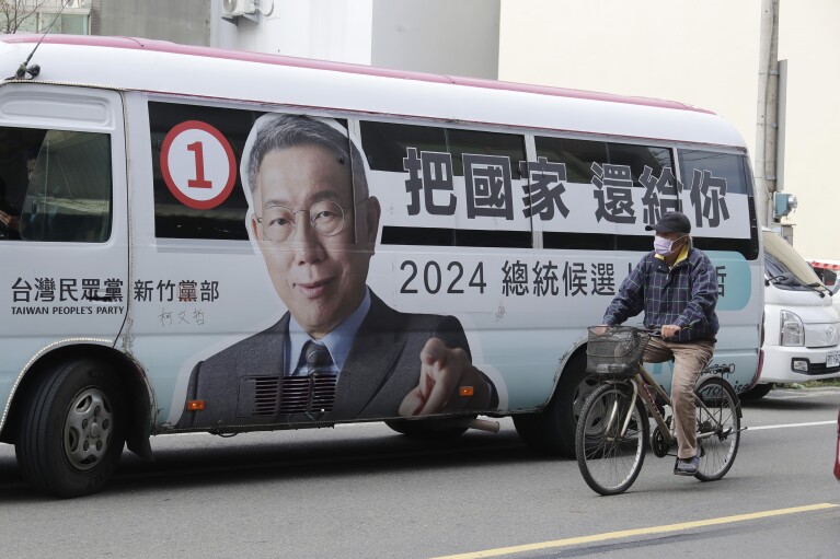 A man rides past a bus with a poster of Taiwan People's Party (TPP) presidential candidate Ko Wen-je running for the Taiwanese presidential election in Xiangshan District, southwest Hsinchu City, Taiwan, Thursday, Jan. 4, 2024. (AP Photo/Chiang Ying-ying, File)