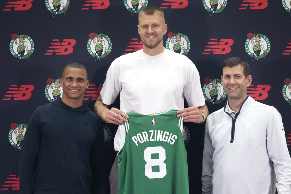FILE - Boston Celtics center Kristaps Porzingis, center, poses with coach Joe Mazzulla, left, and Brad Stevens, president of basketball operations, during a media availability June 29, 2023, in Boston. Porzingis, whom the Celtics acquired in a trade this offseason, will not play for Latvia in the FIBA World Cup because of plantar fasciitis, a foot problem that has lingered. Porzingis announced on X, the social-media platform previously known as Twitter, that he made the decision after an MRI in consultation with the Celtics and Latvian coaching and medical staffs .(Stuart Cahill/The Boston Herald via AP, File)
