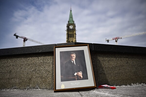 A framed portrait of former Prime Minister Brian Mulroney leans against the Centennial Flame on Parliament Hill as Canadians mourn his death at the age of 84, in Ottawa, Canada on Friday, March 1, 2024. (Justin Tang/The Canadian Press via AP)