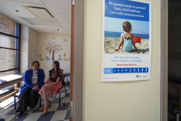 An immunization poster is seen outside of an examination room where Tammy Camp, left, and Summer Davies, both with the Texas Tech University Health Sciences Center, speak to The Associated Press in Lubbock, Texas, Tuesday, Feb. 25, 2025. (AP Photo/Julio Cortez)