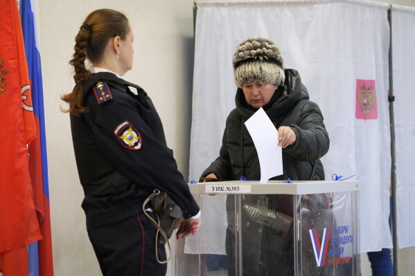 A woman casts a ballot as a police officer guards at a polling station during the presidential election in St. Petersburg, Russia, Sunday, March 17, 2024. Voters in Russia are going to the polls for the last day of a presidential election that is all but certain to extend President Vladimir Putin's rule after he clamped down on dissent. (AP Photo/Dmitri Lovetsky)