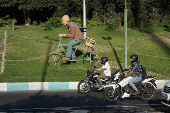 Motorbikes drive past a cyclist statue on a highway in Tehran, Iran, Monday, June 2, 2025. (AP Photo/Vahid Salemi)