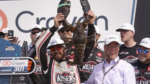 Martin Truex Jr., front left, holds up a lobster while celebrating after his win in the Crayon 301 NASCAR Cup Series race as David McGrath, second from front right, executive vice president and general manager of New Hampshire Motor Speedway, smiles Monday, July 17, 2023, at the speedway in Loudon, N.H. (AP Photo/Steven Senne)