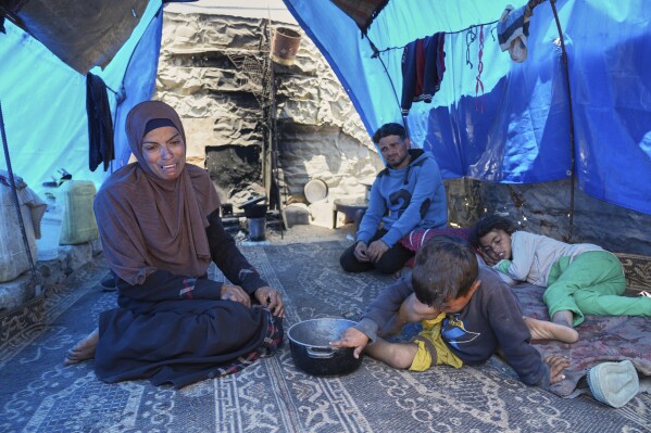Ward Nar, left, reacts as she speaks with the photographer after returning empty-handed from attempting to receive donated food for her family, including her husband Mohammed Zaharna (center right) and their children, Sally (right) and Raed, at a community kitchen in Khan Younis, in the southern Gaza Strip, Friday, May 9, 2025. (AP Photo/Abdel Kareem Hana)