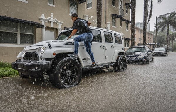 Héctor Guifaro se sube a la parte delantera de su vehículo para evitar una calle inundada frente a St. Edwards Apartments en Edgewater en NE 23rd Street en Miami, el miércoles 12 de junio de 2024.  (Al Díaz/Miami Herald vía AP)