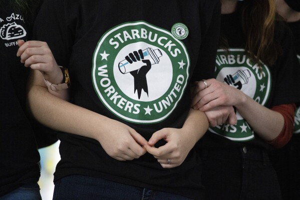 FILE - Starbucks employees and supporters link arms during a union election watch party Dec. 9, 2021, in Buffalo, N.Y. Thousands of U.S. Starbucks workers plan to walk off the job Thursday -- one of the chain's busiest days of the year -- to protest the company's anti-union stance. (AP Photo/Joshua Bessex, File)