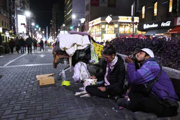Georgina Oliva pets Sol, one of her four dogs, as her partner Carlos Sosa nuzzles with Tinchi, another one of their dogs, as they beg for money in Buenos Aires, Argentina, Sunday, April 27, 2025. (AP Photo/Natacha Pisarenko)