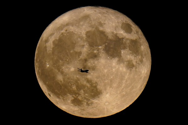 FILE - A plane passes in front of a supermoon, July 13, 2022, in Milwaukee. A rare blue supermoon could normal raise tides just as Hurricane Idalia takes aim at Florida’s west coast, exacerbating flooding from the storm. The moon will be closest to the Earth on Wednesday night, Aug. 30, 2023, the same day Idalia is expected to make landfall in Florida. (AP Photo/Morry Gash, File)