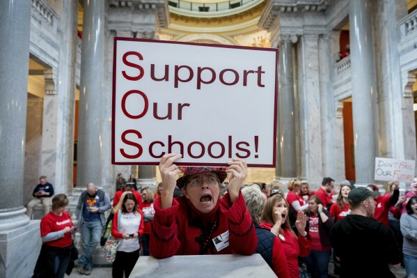 FILE - Karen Schwartz, a teacher at Phoenix School of Discovery in Louisville, stands with other teaches and their supporters to protest perceived attacks on public education on March 12, 2019, in Frankfort, Ky. While 2023 Republican gubernatorial nominee Daniel Cameron has downplayed his support for charter schools and vouchers in presenting his education plans, school choice advocacy groups have pumped millions of dollars into ads attacking his opponent, Democratic Gov. Andy Beshear. (AP Photo/Bryan Woolston, File)