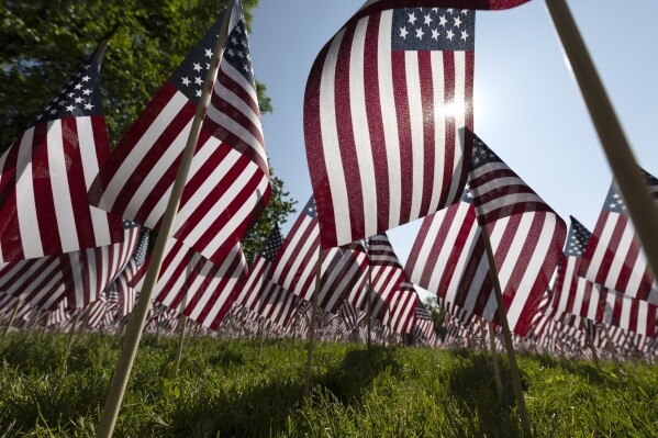 FILE - The sun shines through the flags in the Memorial Day Flag Garden on Boston Common, May 27, 2023, in Boston. Memorial Day is supposed to be about mourning the nation’s fallen service members. But it’s come to anchor the unofficial start of summer and retail discounts. (AP Photo/Michael Dwyer, file)