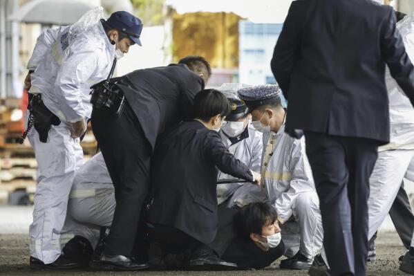 A suspect, center on the ground, is caught by police after he allegedly threw "the suspicious object," as Japanese Prime Minister Fumio Kishida visited Saikazaki port for an election campaign event in Wakayama, western Japan Saturday, April 15, 2023.(Kyodo News via AP, File)