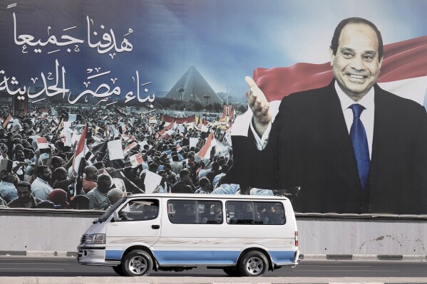 A minibus passes under a billboard supporting Egyptian President Abdel Fattah el-Sissi for the presidential elections, in Cairo, Egypt, Sunday, Dec. 10, 2023. Egyptians began voting Sunday in a presidential election in which el-Sissi, who faces no serious challenger, is certain to win another term, keeping him in power until 2030. The Arabic writing reads: