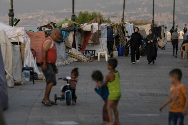 People walk past tents set up as temporary shelters by displaced families fleeing the Israeli airstrikes in the south and Dahiyeh, on Beirut's corniche, Lebanon, Monday, Oct. 14, 2024. (AP Photo/Bilal Hussein)WLD