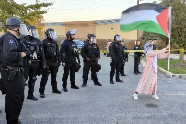 In this image taken from video, a demonstrator waves a Palestinian flag in front of a line of police officers during a pro-Palestinian demonstration Sunday, May 22, 2023, in Skokie, Ill. Cook County prosecutors have charged a 33-year-old man who pepper sprayed demonstrators Sunday at a pro-Palestinian protest near an Israel solidarity event in the Chicago suburbs with two felony hate crimes and two counts of aggravated battery. (AP Photo)