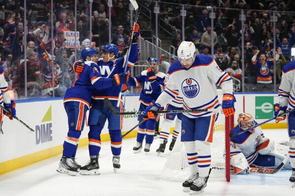 New York Islanders' Anders Lee, second from left, celebrates with Bo Horvat, left, after scoring a goal, while Edmonton Oilers' Stuart Skinner, right, and Cody Ceci, second from right, react during the second period of an NHL hockey game Tuesday, Dec. 19, 2023, in Elmont, N.Y. (AP Photo/Frank Franklin II)