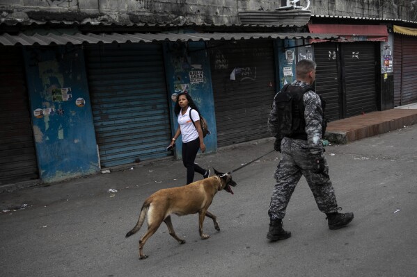 FILE - Police from the Dog Action Battalion patrol the Complexo da Mare favela during an operation targeting drug gangs in Rio de Janeiro, Brazil, Sept. 26, 2022. When Rio state's military police conduct operations and face off with local drug traffickers, class is canceled and kids take shelter at home. (AP Photo/Bruna Prado, File)