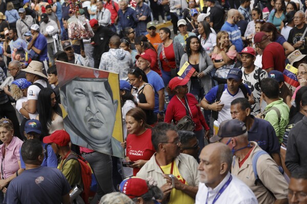 Government supporters hold a painting depicting the late Venezuelan President Hugo Chavez, during an event marking the anniversary of the 1958 coup that overthrew dictator Marcos Perez Jimenez, in Caracas, Venezuela, Tuesday, Jan. 23, 2024. (AP Photo/Jesus Vargas)