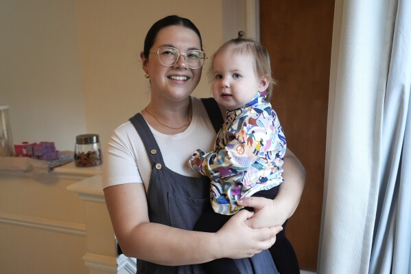 Rachael Lang poses with her daughter, Delaney, 1, in Livonia, Mich., Monday, March 18, 2024. Lang and her husband share DNA and a surname with their daughter. But living in Michigan, the only state where there is a criminal ban on paid surrogacy contracts, has forced the couple to spend close to a year trying to adopt their daughter, who was born through a surrogate due to Lang's past cancer diagnosis. (AP Photo/Paul Sancya)