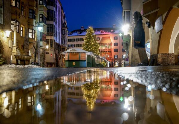 FILE - The Christmas tree of the closed Christmas market is reflected in a puddle in Innsbruck, Austria, Monday, Nov. 29, 2021. As countries shut their doors to foreign tourists or reimpose restrictions because of the new omicron variant of the coronavirus, tourism that was just finding it's footing again could face another major pandemic slowdown amid the uncertainty about the new strain. (Photo/Michael Probst, File)