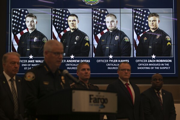 Official portraits of Fargo, N.D., police officers involved in a shooting a day earlier are displayed during a news conference, Saturday, July 15, 2023, at Fargo City Hall. Officer Jake Wallin, far left, was fatally shot. Officers Andrew Dotas and Tyler Hawes were both critically injured. Officer Zachary Robinson, who killed the suspect and is on paid administrative leave, is also pictured. Authorities have said a civilian was also injured. (AP Photo/Ann Arbor Miller )