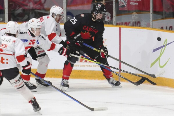 Canada's Matthew Schaefer, right, battles for the puck with Switzerland's Basile Sansonnens, second right, and Eric Schneller (26) during the third period of an IIHF World Junior Hockey Championship pre-tournament game in Ottawa, Ontario, Dec. 19, 2024. (Sean Kilpatrick/The Canadian Press via AP, File)