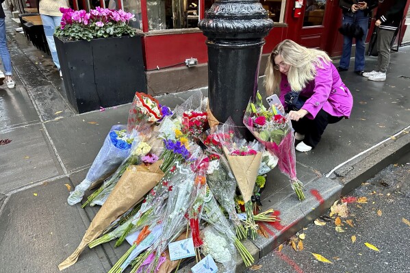 A person takes pictures of a makeshift memorial for Matthew Perry outside the building known as the "Friends" building in New York, Sunday, Oct. 29, 2023. Fans lingered in the rain, taking pictures and leaving flowers on the corner outside the building shown in exterior shots on the popular TV show. Perry, who played Chandler Bing on NBC鈥檚 鈥淔riends鈥� for 10 seasons, was found dead at his Los Angeles home on Saturday. He was 54. (AP Photo/Brooke Lansdale)