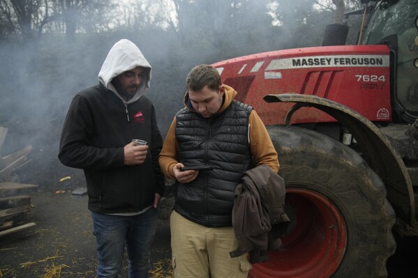 Farmers watch French Prime Minister Gabriel Attal on a smartphone, announcing new measures for farmers, on a blocked highway, Thursday, Feb.1, 2024 in Chilly-Mazarin, south of Paris. Protests have been held across the EU for most of the week and hundreds of angry farmers driving heavy-duty tractors arrived at European Union headquarters, bent on getting their complaints about excessive costs, rules and bureaucracy heard and fixed by EU leaders at a summit Thursday in Brussels, Belgium. (AP Photo/Christophe Ena)