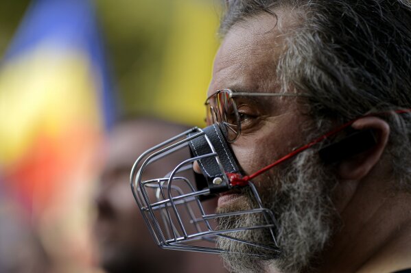 In this photo taken on Saturday, Sept. 19, 2020 a man wears a muzzle during a protest against the COVID-19 pandemic restrictions in Bucharest, Romania. Across the Balkans and the rest of the nations in the southeastern corner of Europe, a vaccination campaign against the coronavirus is overshadowed by heated political debates or conspiracy theories that threaten to thwart the process. In countries like the Czech Republic, Serbia, Bosnia, Romania and Bulgaria, skeptics have ranged from former presidents to top athletes and doctors. Nations that once routinely went through mass inoculations under Communist leaders are deeply split over whether to take the vaccines at all. (AP Photo/Andreea Alexandru)