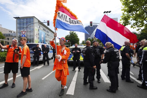 FILE - Netherlands fans walk with flags next to police officers during celebration ahead of a semi final match between Netherlands and England at the Euro 2024 soccer tournament in Dortmund, Germany, Wednesday, July 10, 2024. Germany's top security official says authorities had fewer security problems and crimes to deal with than they expected at the European Championship. The tournament ended on Sunday with Spain beating England 2-1 in the final in Berlin and no reports of serious disturbances. (AP Photo/Markus Schreiber, File)