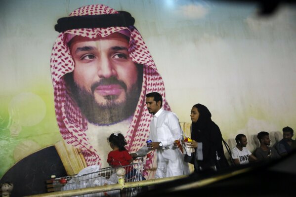 A Saudi family walk past a giant poster of Saudi Crown Prince Mohammed bin Salman, at a shopping mall in  Jiddah, Saudi Arabia, Sunday, Sept. 15, 2019. The weekend drone attack on one of the world's largest crude oil processing plants that dramatically cut into global oil supplies is the most visible sign yet of how Aramco's stability and security is directly linked to that of its owner -- the Saudi government and its ruling family. (AP Photo/Amr Nabil)